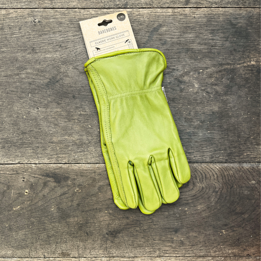 Ein einzelner Barebones Classic Gartenhandschuh aus Büffelleder von Königliche Gartenakademie aus olivgrünem Leder mit einem Pappschild liegt auf einer rustikalen Holzfläche.