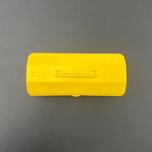 Die gelbe, rechteckige Niwaki Y-Type Toolbox von Niwaki mit Griff und TOOL BOX-Etikett auf dem Deckel steht auf einer dunkelgrauen Oberfläche - perfekt, um Ihre Gartenbedarfsartikel zu organisieren.