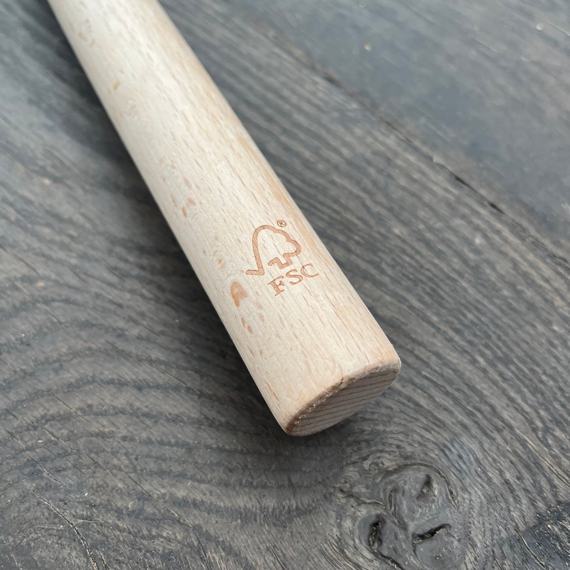 Eine Nahaufnahme der Niwaki FSC Heckenschere von Niwaki zeigt den abgerundeten, aus FSC-zertifiziertem Holz gefertigten und mit dem FSC-Logo gravierten Holzgriff, der auf einer dunklen, strukturierten Holzoberfläche liegt.