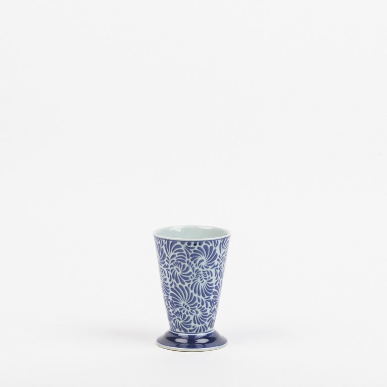 Eine kleine blau-weiß gemusterte Keramikvase von Des Pots by Des Pots, mit ausgestelltem Sockel und floralem Muster auf weißem Hintergrund.
