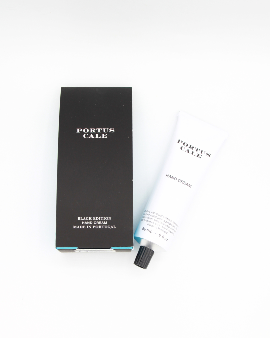Eine schwarze rechteckige Castelbel Handcreme Portus Cale 60 ml - Black Edition Schachtel steht neben einer weißen Feuchtigkeits-Tube mit schwarzem Verschluss, beide auf weißem Hintergrund.