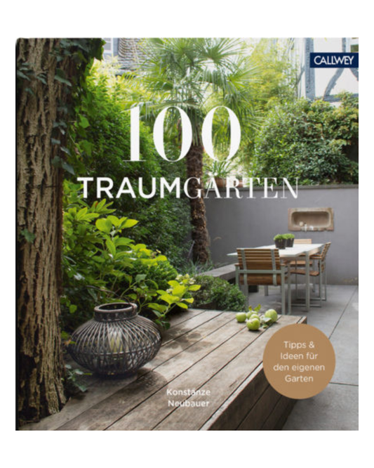 Das Cover von 100 Traumgärten | Faszinierende Privatgärten aus dem Callway Verlag zeigt einen üppigen grünen Garten mit grünen Pflanzen, einem Holztisch und Stühlen sowie einer Laterne auf einer Bank. Autorin: Konstanze Neubauer.