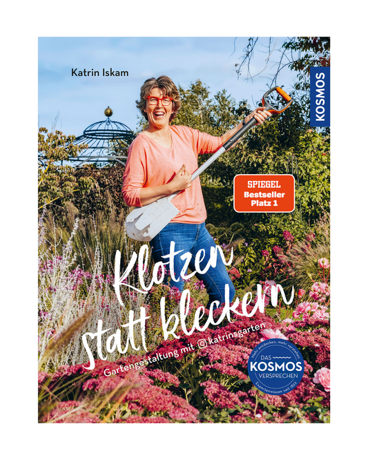 Eine lächelnde Frau in einem korallenroten Pullover und Jeans steht mit einem weißen Spaten in einem lebendigen Garten. Der deutsche Text lautet: Klotzen statt kleckern. Produkt: Klotzen statt kleckern | Gartengestaltung mit Katrin Iskam von Kosmos Verlag.