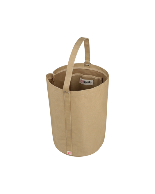 Die Kantan Werkzeugtasche - Niwaki von Königliche Gartenakademie ist eine hellbraune Werkzeugtasche aus Segeltuch mit einem stabilen Griff, einer Außentasche und einer Innentasche mit dem Niwaki-Label. Die Tasche steht aufrecht auf einem weißen Hintergrund.