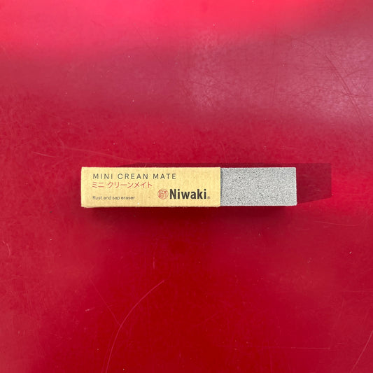 Ein Niwaki - Mini Crean Mate Rost- und Saftradierer mit beigem Etikett und grauem Radiergummi ruht auf einer roten Oberfläche. Ideal für die Reinigung Gartenscheren, sein Etikett verfügt über Englisch und Japanisch Text. Marke: Niwaki.