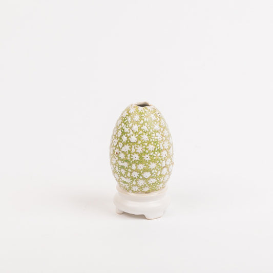 Die Vase von Des pots | Ei-auf-Schale Form Groß der Königlichen Gartenakademie mit grünem Hintergrund und weißem Blumenmuster wird auf einem kurzen weißen Sockel vor einem schlichten weißen Hintergrund präsentiert.