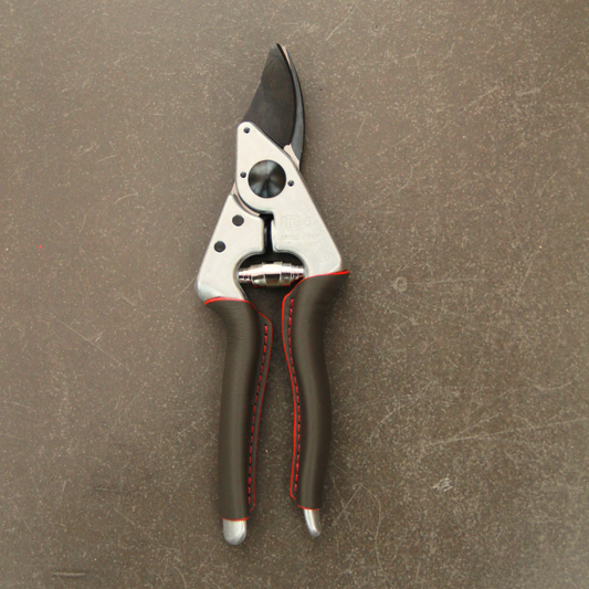 Die Felco 6 ELITE Gartenschere überzeugt durch ihr ergonomisches Design, schwarze Klingen und rote Nähte an den Griffen. Die kompakte Schere der Marke Felco besticht auf schlichter brauner Fläche.