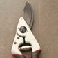 Eine Nahaufnahme der Felco 8 ELITE Gartenschere von Felco mit schwarzen und roten Griffen und der Aufschrift "FELCO 8 SWISS MADE", die auf einer braunen Oberfläche liegt.