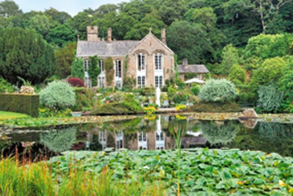 Ein Steinhaus mit gewölbten Fenstern steht inmitten von Gärten, die von "Gärtnern wie Gott in England" aus dem Callwey Verlag inspiriert sind, und spiegelt sich in einem Seerosenteich.