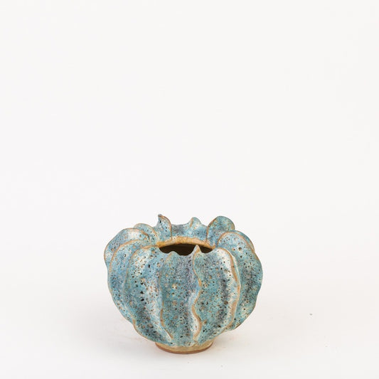 Die Vase von Des Pots | Moos Klein in Blaugrün von Des Pots ist eine kleine, runde, handgeformte Steingutvase mit wellenförmigem Rand und strukturierter blaugrüner Glasur, kürbisähnlich geformt auf weißem Hintergrund.