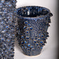 Die Vase | Blau skulptural L von Des Pots ist eine handgefertigte Steinzeugvase mit glänzender, tiefblauer Glasur und erhabenen blau-weißen Blumenmustern sowie dichter, strukturierter Oberfläche.