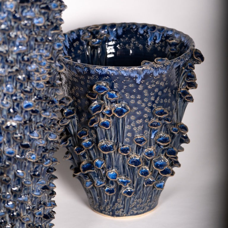 Die Vase | Blau skulptural L von Des Pots ist eine handgefertigte Steinzeugvase mit glänzender, tiefblauer Glasur und erhabenen blau-weißen Blumenmustern sowie dichter, strukturierter Oberfläche.