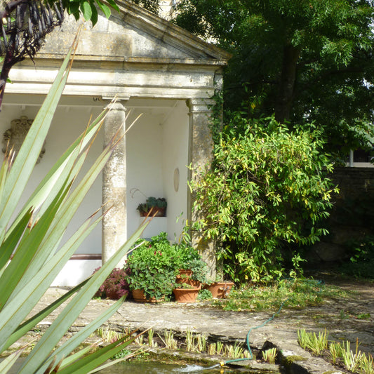 Genießen Sie den Charme der Gärten der Cotswolds mit Isabelle Van Groeningen's Di. 16.09.2025 | 14.30-16.00 AFTERNOON TEA VORTRAG, inspiriert von üppigen Gärten, grünen Pflanzen und bunten Blumen auf einer sonnigen, gepflasterten Terrasse.