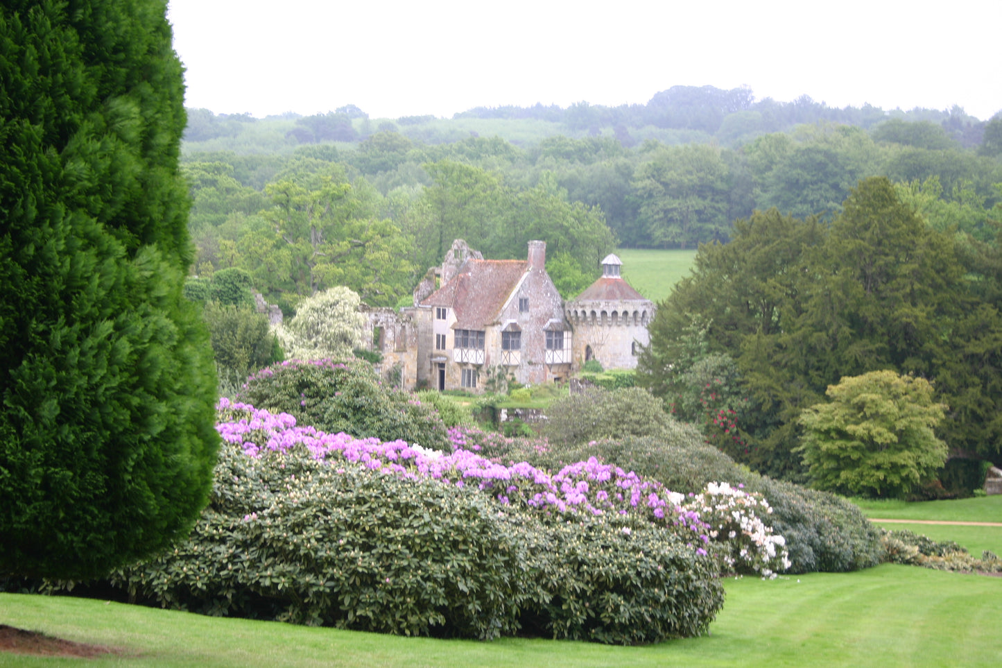 Ein steinernes Herrenhaus mit rotem Ziegeldach, eingebettet in üppiges Grün, erinnert an den Charme der Gärten von Kent und Sussex - ideal für Dr. Isabelle Van Groeningens "Di. 17.02.2026 | 14.30-15.30 AFTERNOON-TEA-VORTRAG Die Gartenpracht von Kent und Sussex.