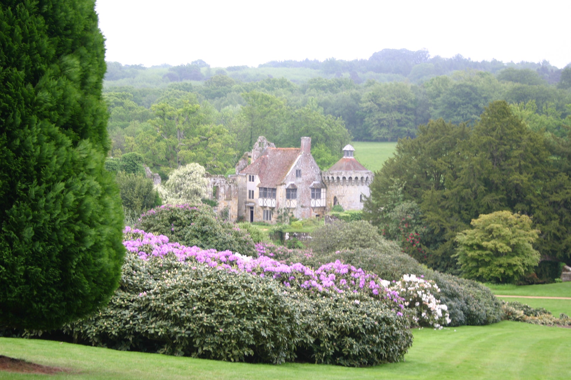 Ein steinernes Herrenhaus mit rotem Ziegeldach, eingebettet in üppiges Grün, erinnert an den Charme der Gärten von Kent und Sussex - ideal für Dr. Isabelle Van Groeningens "Di. 17.02.2026 | 14.30-15.30 AFTERNOON-TEA-VORTRAG Die Gartenpracht von Kent und Sussex.