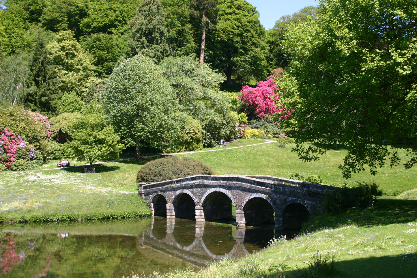 Eine Steinbrücke mit drei Bögen überspannt einen ruhigen Teich in üppigem Grün, der den Charme der Gärten von Somerset, Dorset und Wiltshire widerspiegelt - zu sehen in Dr. Isabelle Van Groeningens Afternoon-Tea-Vortrag am 17.03.2026 um 14:30 Uhr.