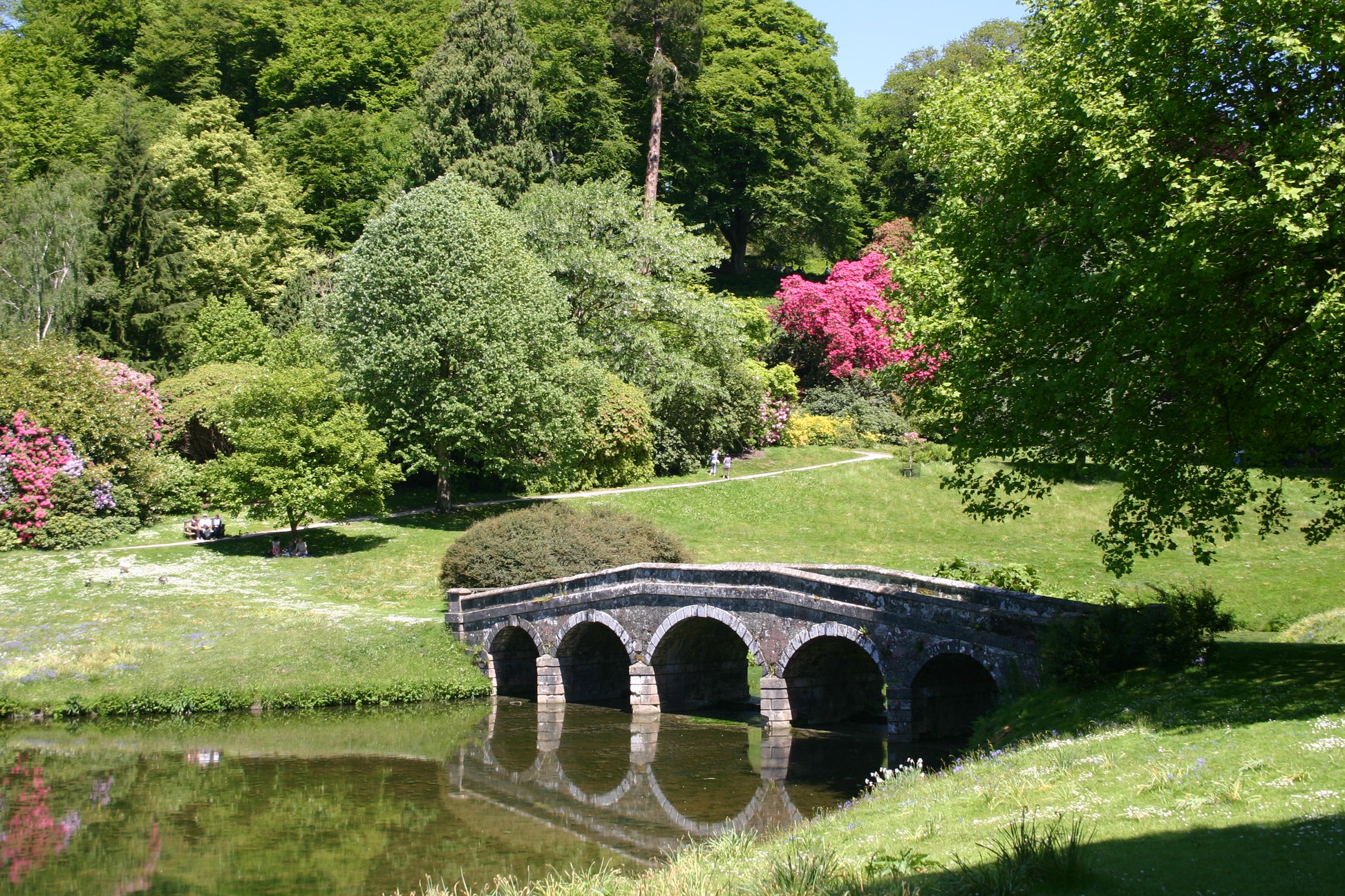 Eine Steinbrücke mit drei Bögen überspannt einen ruhigen Teich in üppigem Grün, der den Charme der Gärten von Somerset, Dorset und Wiltshire widerspiegelt - zu sehen in Dr. Isabelle Van Groeningens Afternoon-Tea-Vortrag am 17.03.2026 um 14:30 Uhr.