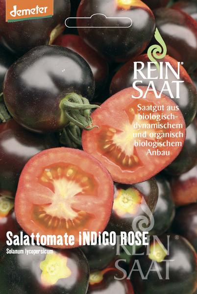 Eine Packung Reinsaat Salattomate 'Indigo Rose' Samen, Tomatenspezialität: dunkelblau-violett, mit ganzen und halbierten Tomaten, die ihr leuchtend rotes Inneres zeigen. Der Text ist auf Deutsch.