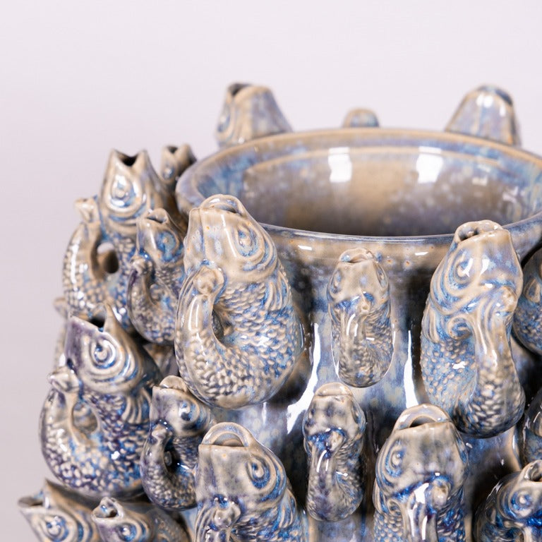 Die Vase von Des Pots aus Steingut, Modell 'Fisch' Groß in Blau, ist glasiert und mit vielen plastischen blauen und grauen Fischköpfen verziert, die dicht nebeneinander auf der Oberfläche angeordnet sind.
