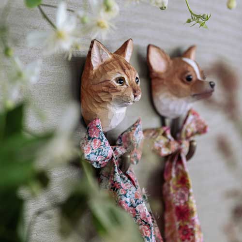 Zwei Wildlife Garden Handgeschnitzter Wandhaken aus Holz | Hauskatze in Form einer orangefarbenen Katze oder eines braun-weißen Hundes mit Blumenschleifen sind an einer hellen Wand angebracht. Ein einzigartiges Geschenk für Tierliebhaber!.