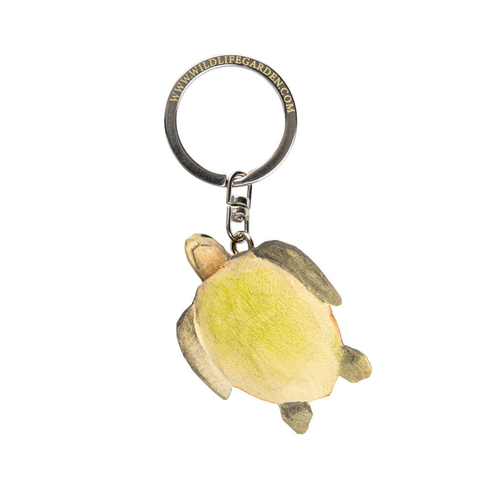 Der handgefertigte Schlüsselanhänger aus Holz | Schildkröte von Wildlife Garden zeigt einen handgeschnitzten, grün-braun bemalten Holz-Schildkröten-Anhänger an einem Metallring, fotografiert aus der Vogelperspektive auf weißem Hintergrund.