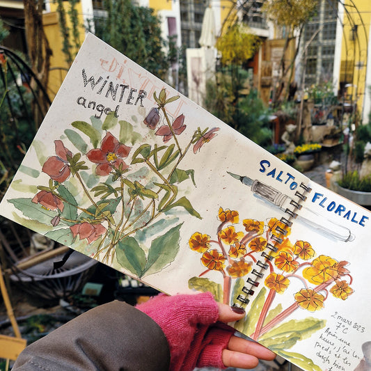 Eine Hand in einem rosa Handschuh hält ein aufgeschlagenes Skizzenbuch mit Blumenaquarellen - eine ideale Inspiration für dein Gartentagebuch oder für den Fr. 05.09.2025 | 10-13 Uhr AQUARELLWORKSHOP - Mein Gartentagebuch bei Königliche Gartenakademie mit Stéphanie Weppelmann.