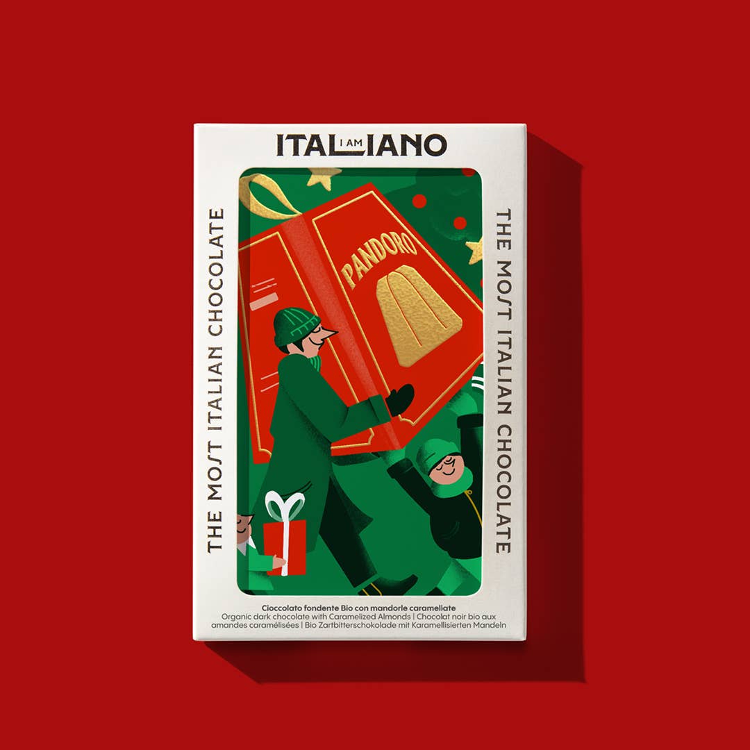 Eine Schachtel I AM ITALIANO Bio-Dunkle-Schokolade-Pandoro mit Mandel mit zwei Personen, die einen großen Pandoro, eine Geschenkschachtel und Weihnachtsschmuck auf Rot tragen. Text: DIE ITALIENISCHSTE SCHOKOLADE. Marke: I AM ITALIANO.