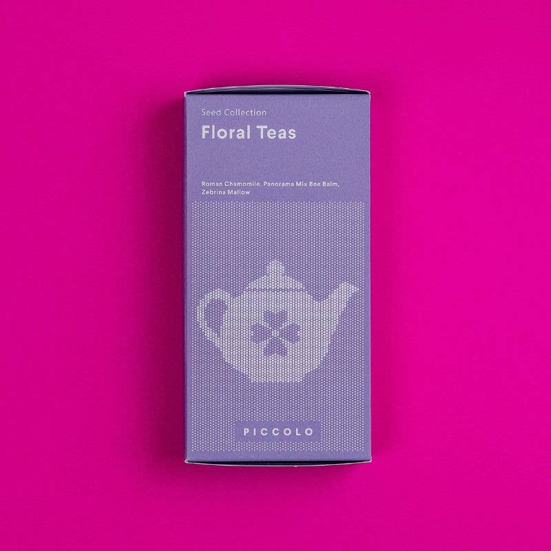 Eine lilafarbene Schachtel mit der Aufschrift Piccolo Seeds | Kollektion "Tees mit Blumen", auf der gentechnikfreie Kamille Samen und eine gepunktete Teekanne abgebildet sind, steht vor einem leuchtend rosa Hintergrund. Teil der Piccolo Seeds Kollektion.
