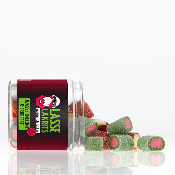 Ein durchsichtiges Glas von LASSE LAKRITS mit der Aufschrift "natürlich lecker" liegt auf der Seite und verschüttet zuckerüberzogene Saure Wassermelone & Saure Erdbeere Fruchtgummi auf einer weißen Fläche - lorbeerförmige Bonbons mit rosa Kern, ganz ohne Palmöl.