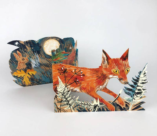 Die Fuchs Collage Karte von Mark Hearld by Art Angels zeigt einen roten Fuchs mit gelben Augen inmitten von Farnen und einen weiteren Fuchs unter einem Vollmond in einem sternenklaren Nachthimmel, der Hearlds unverwechselbaren Collage-Stil einfängt.
