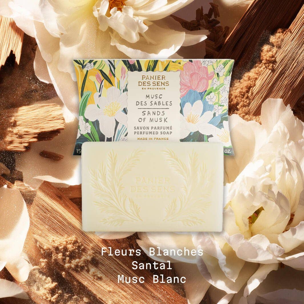 Eine florale Schachtel und ein geprägter Panier Des Sens Duftseife | Musc des Sables 150 g Barren sind auf einem weichen weißen Blumenhintergrund abgebildet. Der Text lautet: Fleurs Blanches, Santal, Musc Blanc.