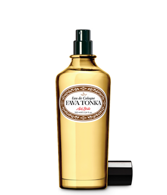 Der goldgelbe Glasflakon von Ach.Brito - Eau de Cologne - Fava Tonka 100 ml hat einen schwarzen Sprühkopf, ein weißes Etikett mit dunkler Schrift und eine Kappe daneben, die den einzigartigen Tonkabohnen-Duft dieses Ach.Brito-Duftes hervorhebt.