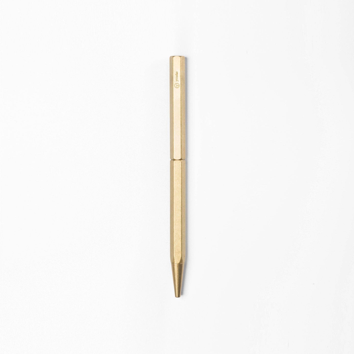 Der ENTREPÔT - YSTUDIO Klassischer Revolve Kugelschreiber Schlank mit einem goldenen sechseckigen Messingkörper steht senkrecht vor einem schlichten weißen Hintergrund.