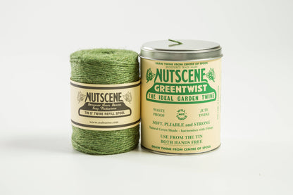 Eine Spule mit dreilagigem Jutegarn und eine Metalldose mit der Aufschrift „Nutscene Twines Ltd – Iconic Tin of Nutscene Twine – Schnur in einer Dose (490 Fuß)“ von Nutscene Twines Ltd liegen auf einem schlichten weißen Hintergrund.