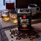Eine Dose Brady's Coffee Company - Brady's Kaffeedose mit ganzen Bohnen, im Fass gereift, irischer Whiskey steht auf einem rustikalen Holztisch, umgeben von ganzen Bohnen, zwei Gläsern Whiskykaffee und einem schwarzen Becher im Hintergrund.