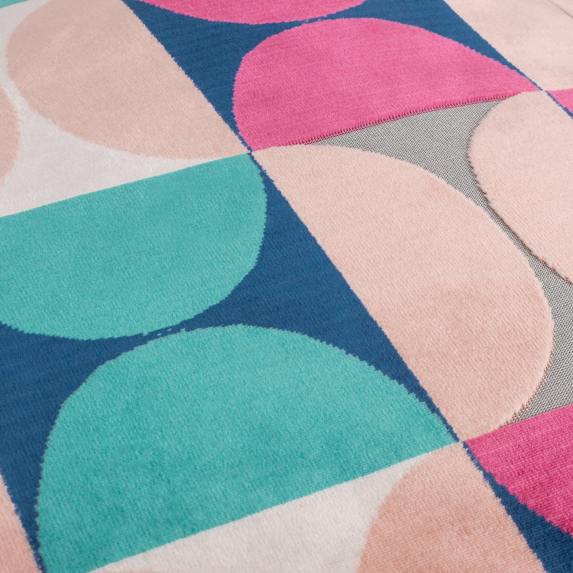 Eine Nahaufnahme des Riva Home Samtkissens im Bardot-Schliff Magenta/Blau zeigt überlappende Halbkreise in Magenta und Blau, die ein lebendiges, geometrisches Design bilden, das von Juwelentönen inspiriert ist.
