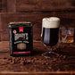 Ein Glas Irish Coffee mit Sahne steht neben der Brady's Coffee Company Kaffeedose mit ganzen Bohnen, im Fass gereift, irischer Whiskey; umgeben von Bohnen, mit einem Glas Whiskey im Hintergrund.