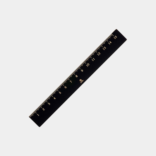 Das ENTREPÔT - YSTUDIO Klassischer Reflect Lineal aus schwarzem Messing mit goldenen Markierungen (0-15 cm) ist ein elegantes Designer-Büroaccessoire und liegt diagonal auf schlicht weißem Hintergrund.