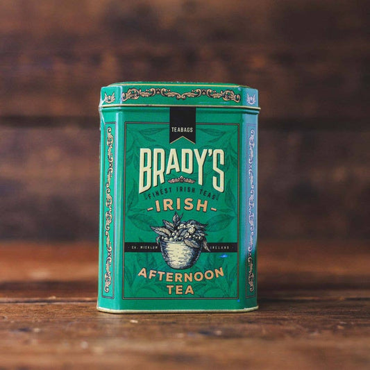 Eine grüne Dose Brady's Coffee Company – Bradys irischer Nachmittagstee zeigt blaue und goldene Akzente, eine Teekannenillustration und das Versprechen „irischer Geschmack“ auf einer Holzoberfläche mit unscharfem Hintergrund.