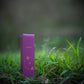 Eine lilafarbene, rechteckige H&B-Weihrauchdose mit der Aufschrift "Natürlicher Jasmin-Weihrauch" steht aufrecht auf grünem Gras mit einem unscharfen natürlichen Hintergrund, der die Essenz von aromatischen Pflanzen und reinem Jasmin einfängt.