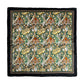Das Koustrupco Seidenschal Morris Windrush grün (50 x 50 cm) zeigt ein kompliziertes Batikmuster mit Vögeln, Blättern und Blumen in Orange, Grün, Senfgelb und Weiß - umrahmt von einer schwarz-braunen Bordüre für einen luxuriösen Touch.
