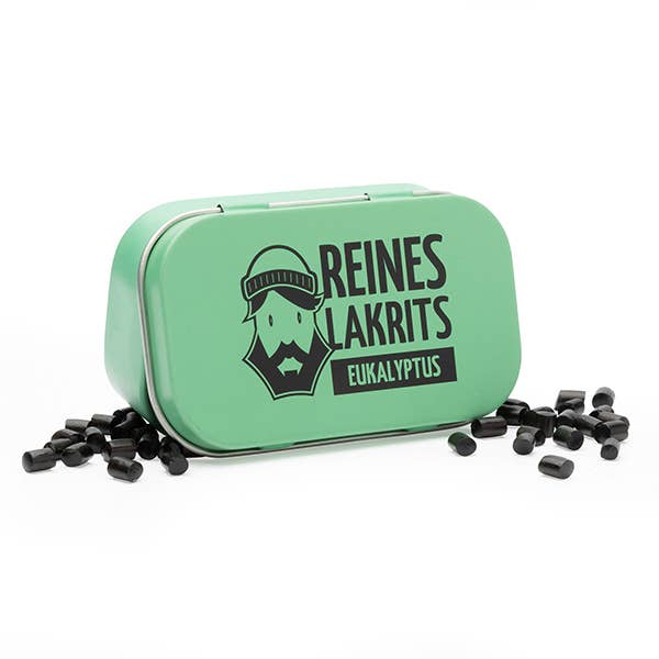 Eine grüne Metalldose mit der Aufschrift "LASSE LAKRITS - natürlich lecker - Dose Reines Lakrits Eukalyptus", auf der ein bärtiger Mann abgebildet ist, wird mit verstreuten kleinen schwarzen zuckerfreien Lakritz-Bonbons auf weißem Hintergrund gezeigt.