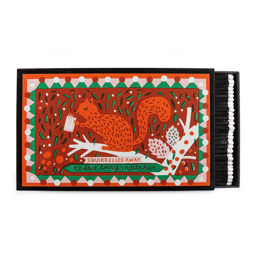 Die Archivist Gallery | Squirrelled Away Giant quadratische Streichholzschachteln zeigen ein rotes Eichhörnchen mit einem Streichholz und buntem Laub. Auf dem Etikett der Schachtel steht "Squirreled away extra long matches" und im Inneren befinden sich schwarze Streichhölzer.