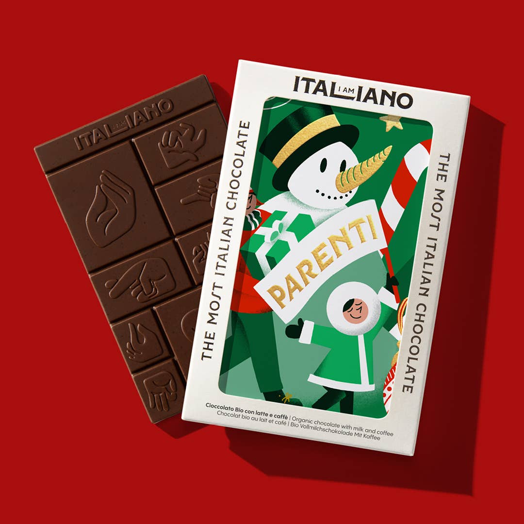 Ein Bio-Schokoladenriegel von I AM ITALIANO - Parenti mit Milch und Kaffee liegt neben einer Box mit Schneemann- und Winterkind-Illustration, beschriftet mit "I AM ITALIANO" und "THE MOST ITALIAN CHOCOLATE".