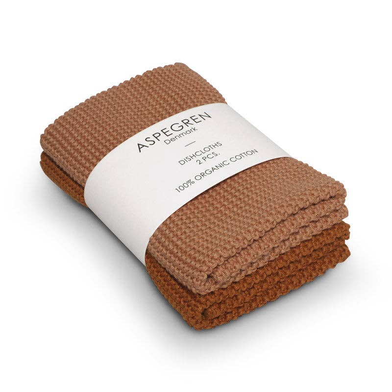 Ein Set aus zwei kürbisfarbenen, gestrickten Spültüchern von Aspegren Denmark aus 100 % Bio-Baumwolle, gefaltet und verpackt mit einem weißen Etikett mit der Aufschrift „DISHLOTHS 2 PCS 100 % ORGANIC COTTON“.
