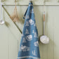 Das Geschirrtuch Sylvie Thiriez - Torchon Jacquard Coeur Vallée Blau aus OEKO-TEX-zertifizierter Baumwolle mit weißen Hütten- und Baummotiven hängt an einer hellgrünen Wand neben Küchenutensilien und getrockneten Kräutern.