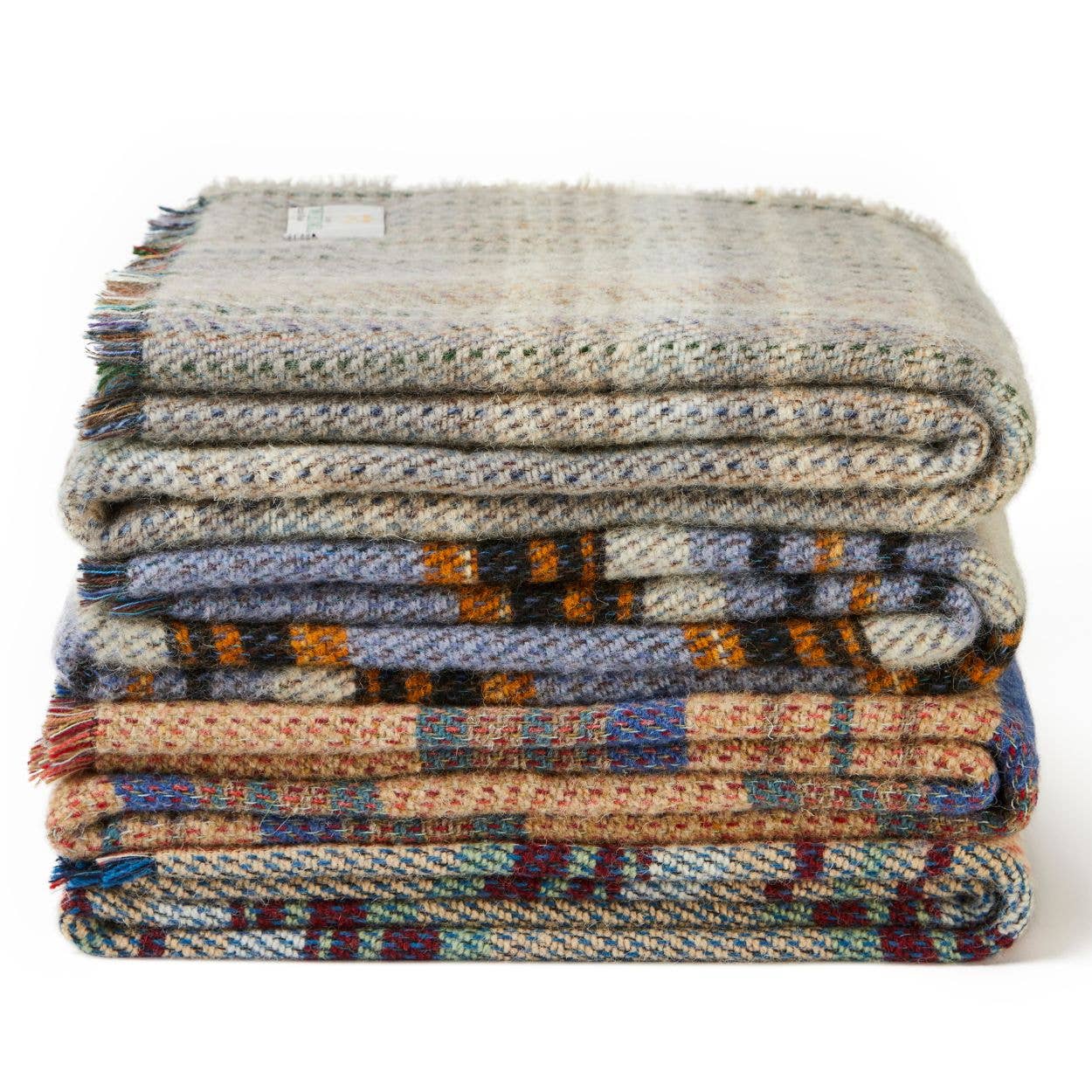 Ein Stapel von vier Tweedmill Textiles Zufällige recycelte Wolldecke - Groß in verschiedenen Beige-, Grau-, Blau- und Rotmustern, hergestellt in Großbritannien, ausgestellt vor einem weißen Hintergrund.