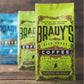 Im Fokus steht eine grüne Tüte Brady's Coffee Company - Brady's Celtic Blend Kaffee, dahinter zwei unscharfe Tüten der Brady's Coffee Company. Auf der Vorderseite der Verpackung sind die Namen Irish Roast, Ballyknocken und Spezialitätenqualität zu sehen.