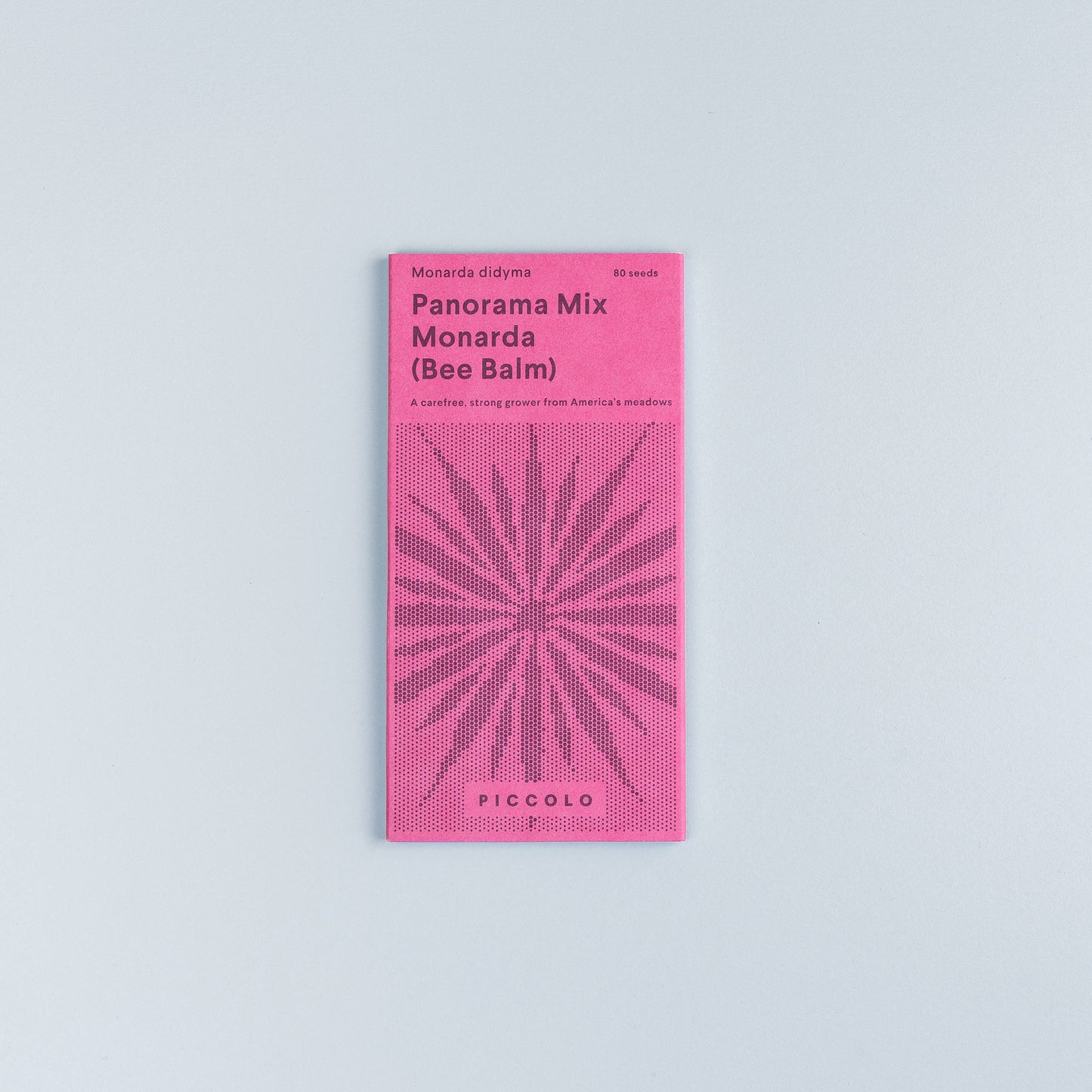 Eine rosa Piccolo Seeds-Packung mit der Aufschrift "Monarda Panorama-Mix" zeigt eine stilisierte Pflanzenillustration, gibt 80 Samen an und zeigt die Marke Piccolo Seeds am unteren Rand. Das Päckchen steht auf einem hellgrauen Hintergrund.