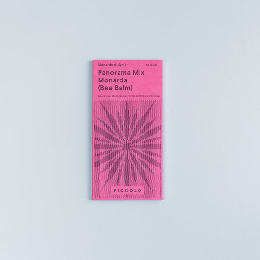 Eine rosa Piccolo Seeds-Packung mit der Aufschrift "Monarda Panorama-Mix" zeigt eine stilisierte Pflanzenillustration, gibt 80 Samen an und zeigt die Marke Piccolo Seeds am unteren Rand. Das Päckchen steht auf einem hellgrauen Hintergrund.